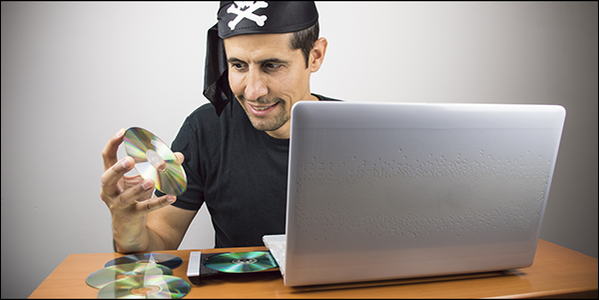 A man dressed as a pirate smiling as he places CD's inside of his laptop.