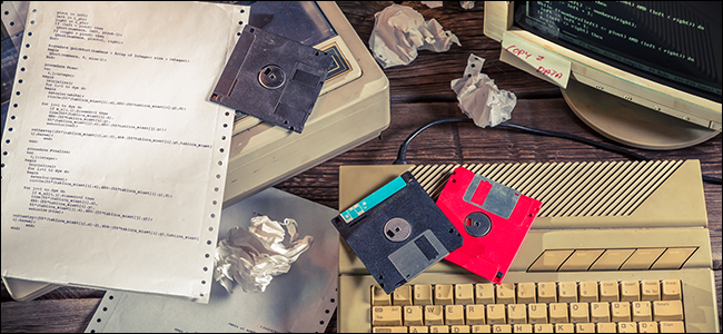 A desk full of floppy disks, old computer hardware, and crumpled up paper.