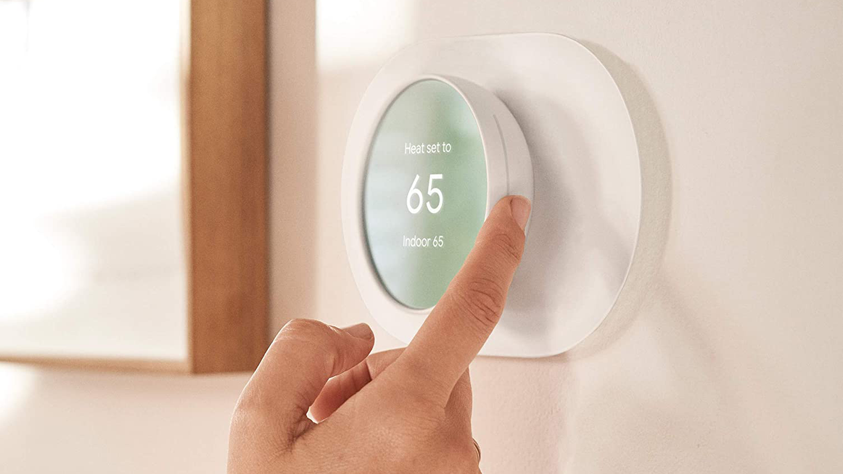 Uma pessoa ajustando um termostato inteligente Google Nest com o dedo.