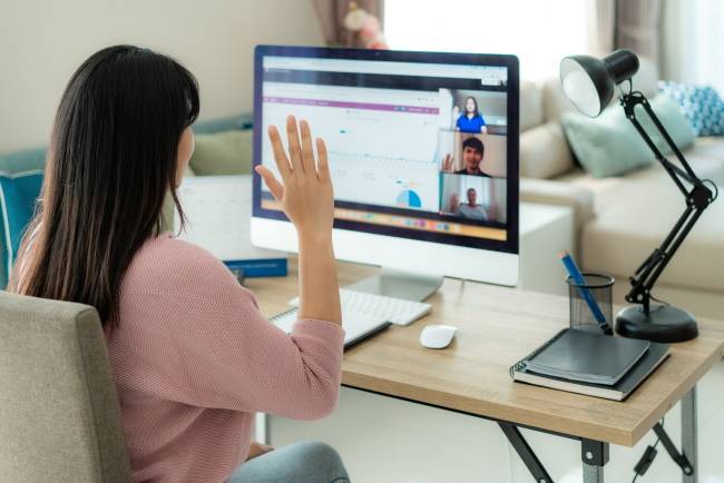 A woman waving at a computer during a video call.