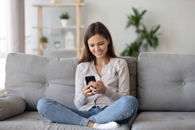 Teenage girl smiling and sitting on couch with smartphone.