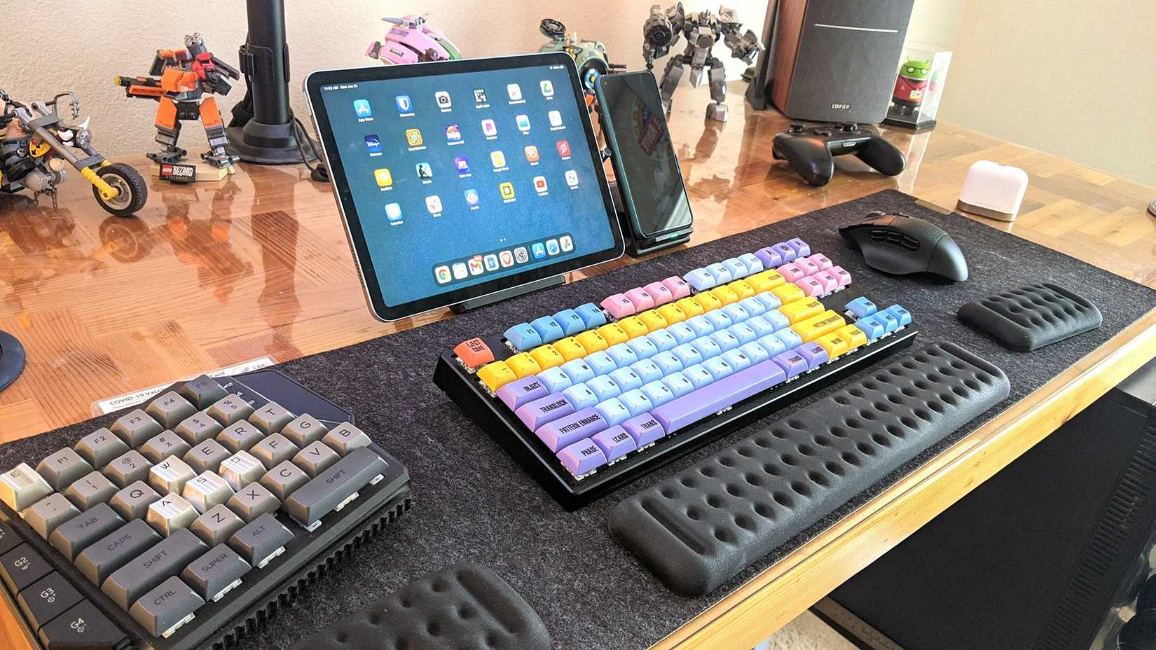 A desk with a keyboard, game pad, mouse, wrist rests, tablet, and phone.
