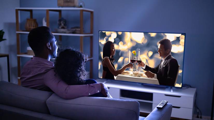 Two young couple watch a movie on a big TV in a modern house.