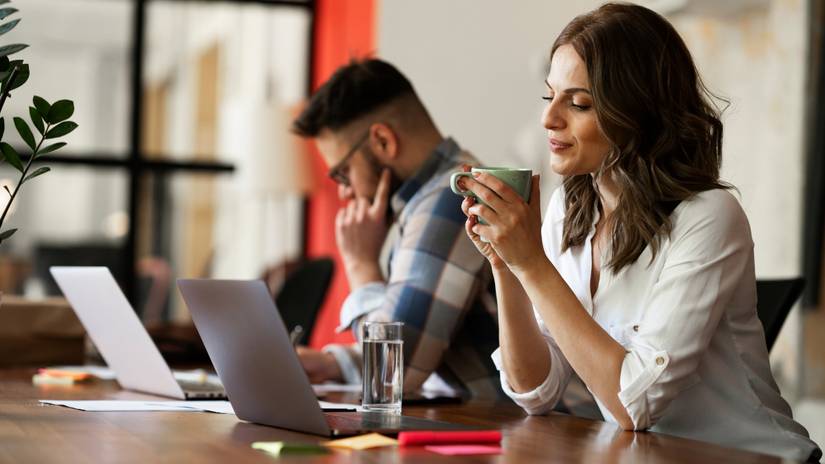 Woman smiling and holding coffee while watching laptop screen