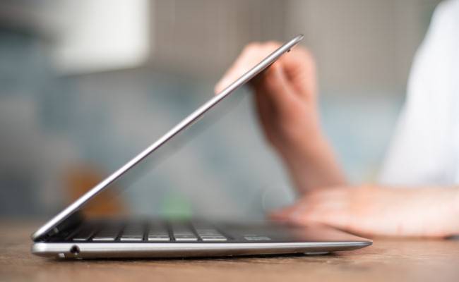 A person closing or opening the lid of a laptop.