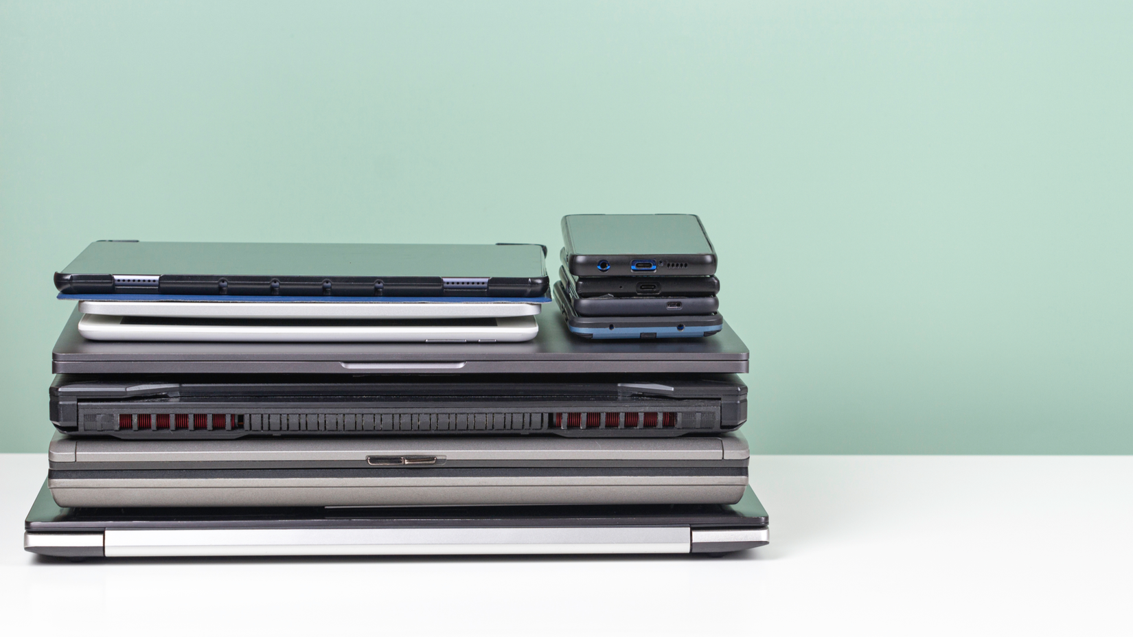 A pile of old used laptop computers, digital tablets, smartphones for recycling on white table. Planned obsolescence, e-waste, electronic waste for reuse and recycle concept.