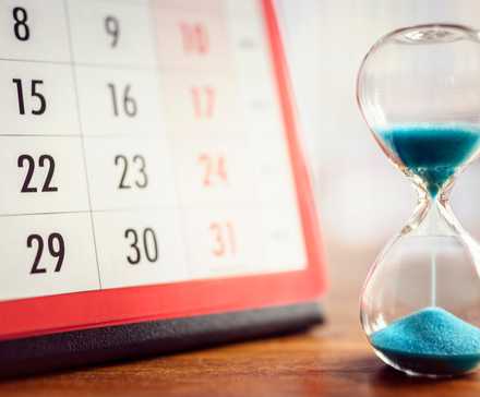 An hourglass on a tabletop next to a calendar.