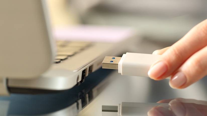 Close-up of a woman's hand connecting a USB drive to a laptop.