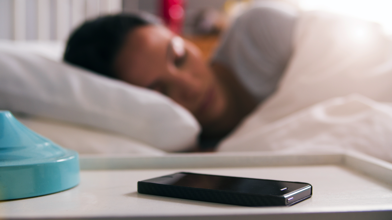 A woman in bed asleep, with her phone on the night stand.