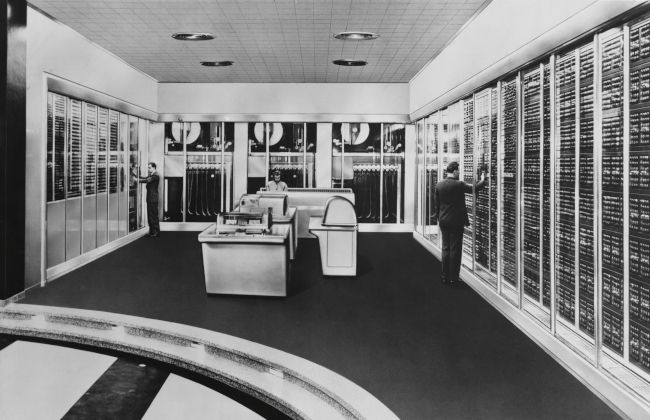 Black and white photo of people working on a mid-century mainframe computer.