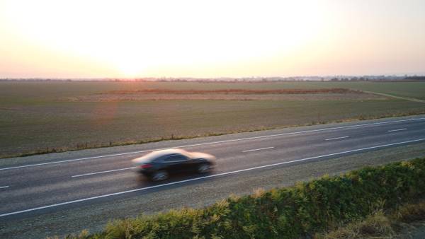 Aerial view of an electric vehicle speeding down a highway crossing throw an open field at sunset.