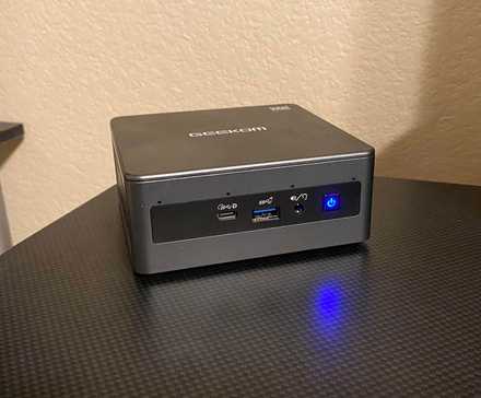 GEEKOM Mini IT11 PC front-facing on a black desktop.