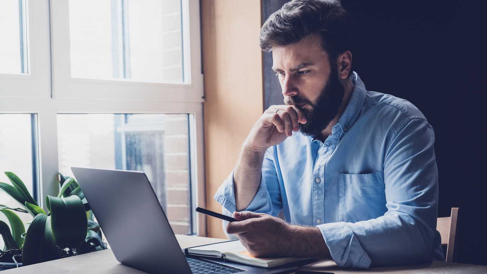 Homem pensando e olhando para um laptop.