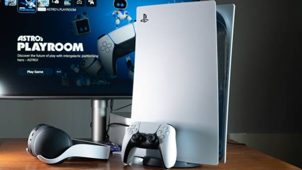 A Sony PlayStation 5 console on a desk with a controller, headphones, and monitor.