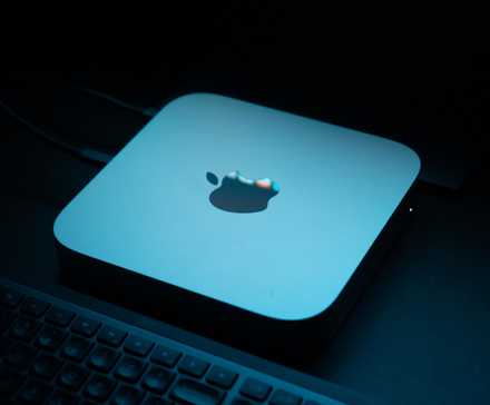 Mac mini на столе в тёмной комнате с голубой подсветкой.