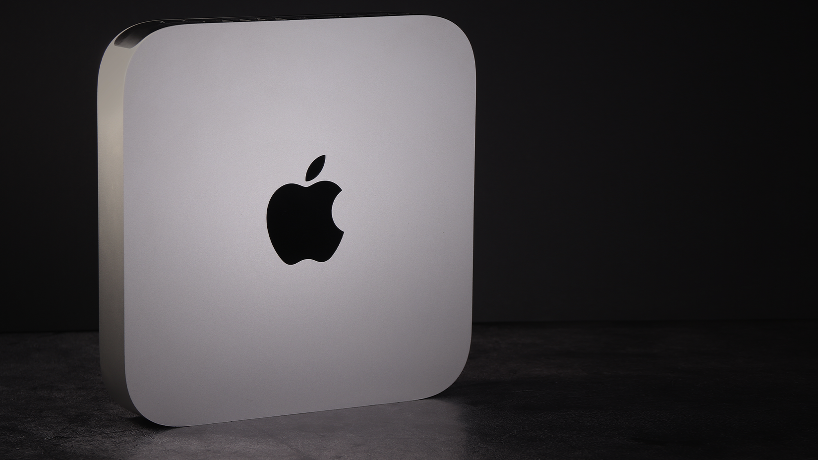 A Mac Mini standing on its side on a dark background.
