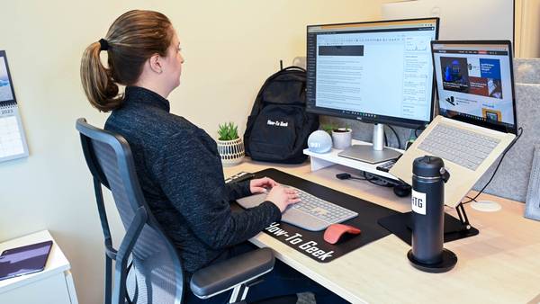 Person typing at a desk with an external monitor connected to a laptop.