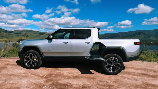 Rivian R1T in front of a lake with the gear tunnel door open. 