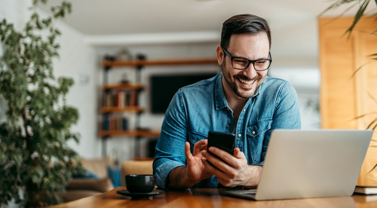 Man sitting at a laptop and scrolling on his smartphone