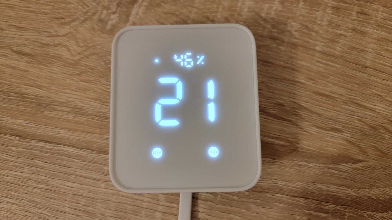 SwitchBot Hub 2 on wood table showing temperature and humidity.