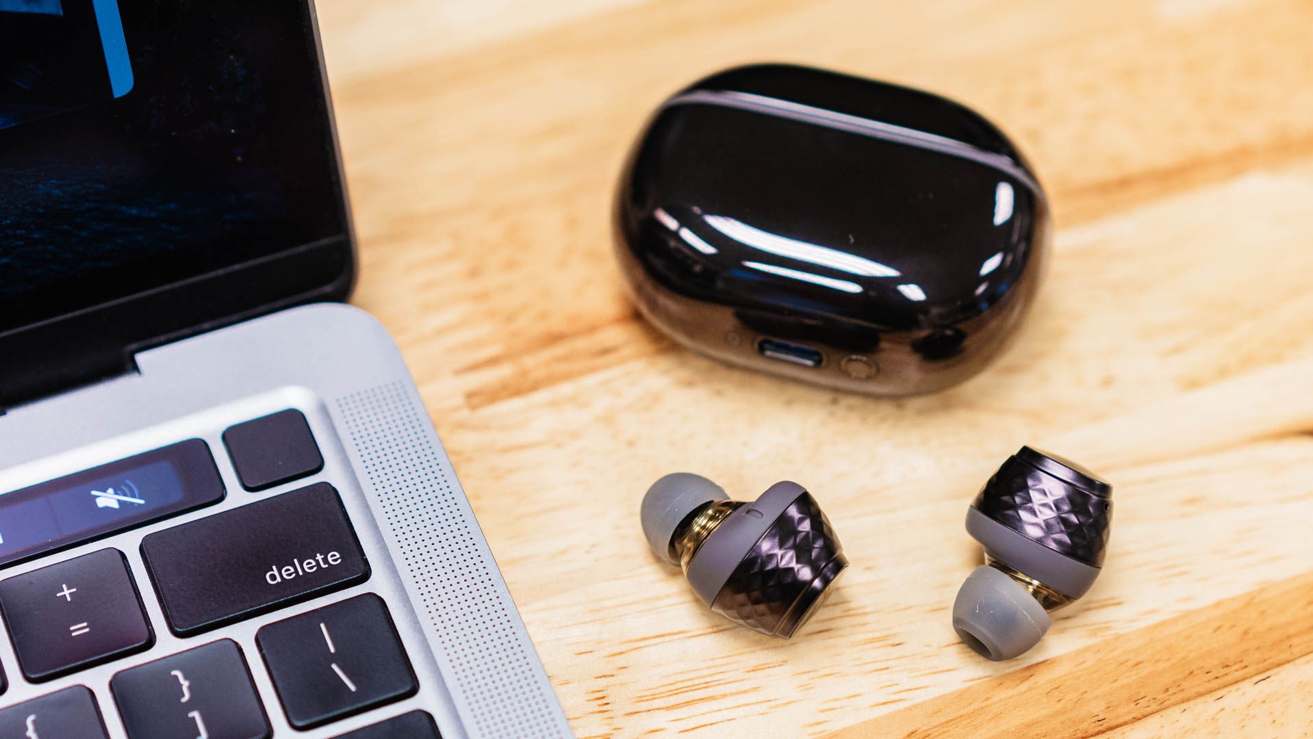 The SoundPeats Engine 4 earbuds and case placed next to a MacBook Pro.