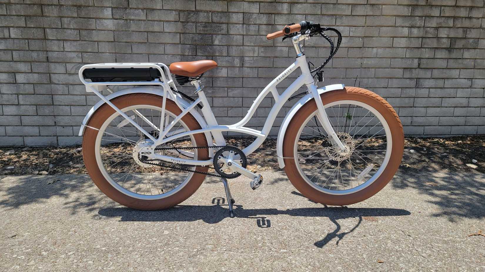 white priority bicycles ride in front of a brick wall.