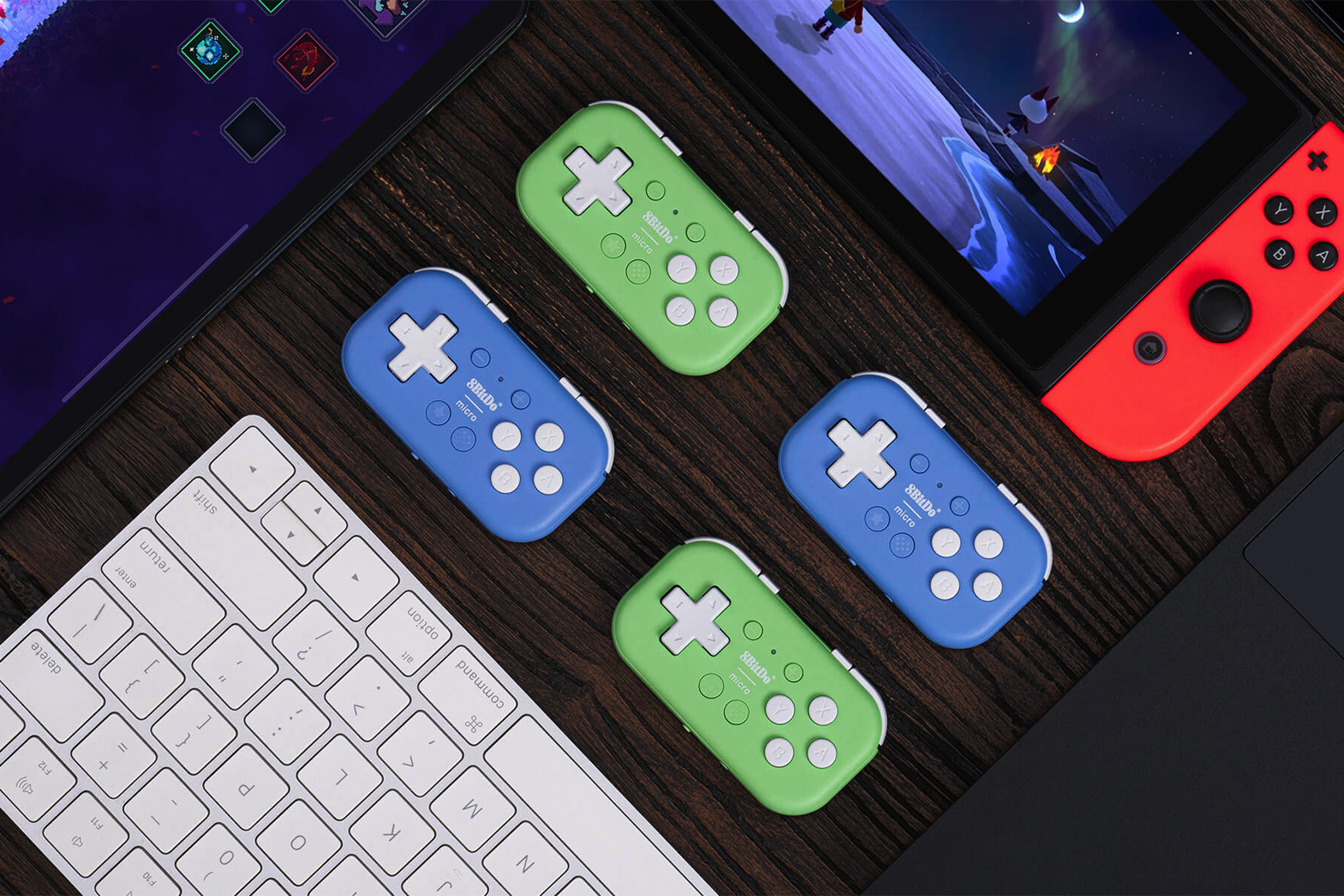 The 8BitDo Micro gamepad surrounded by a Nintendo Switch, iPad, and keyboard.