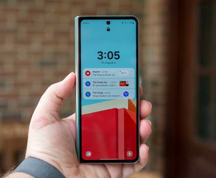 Человек держит в руках Samsung Galaxy Z Fold 5 в закрытом виде с включённым экраном блокировки