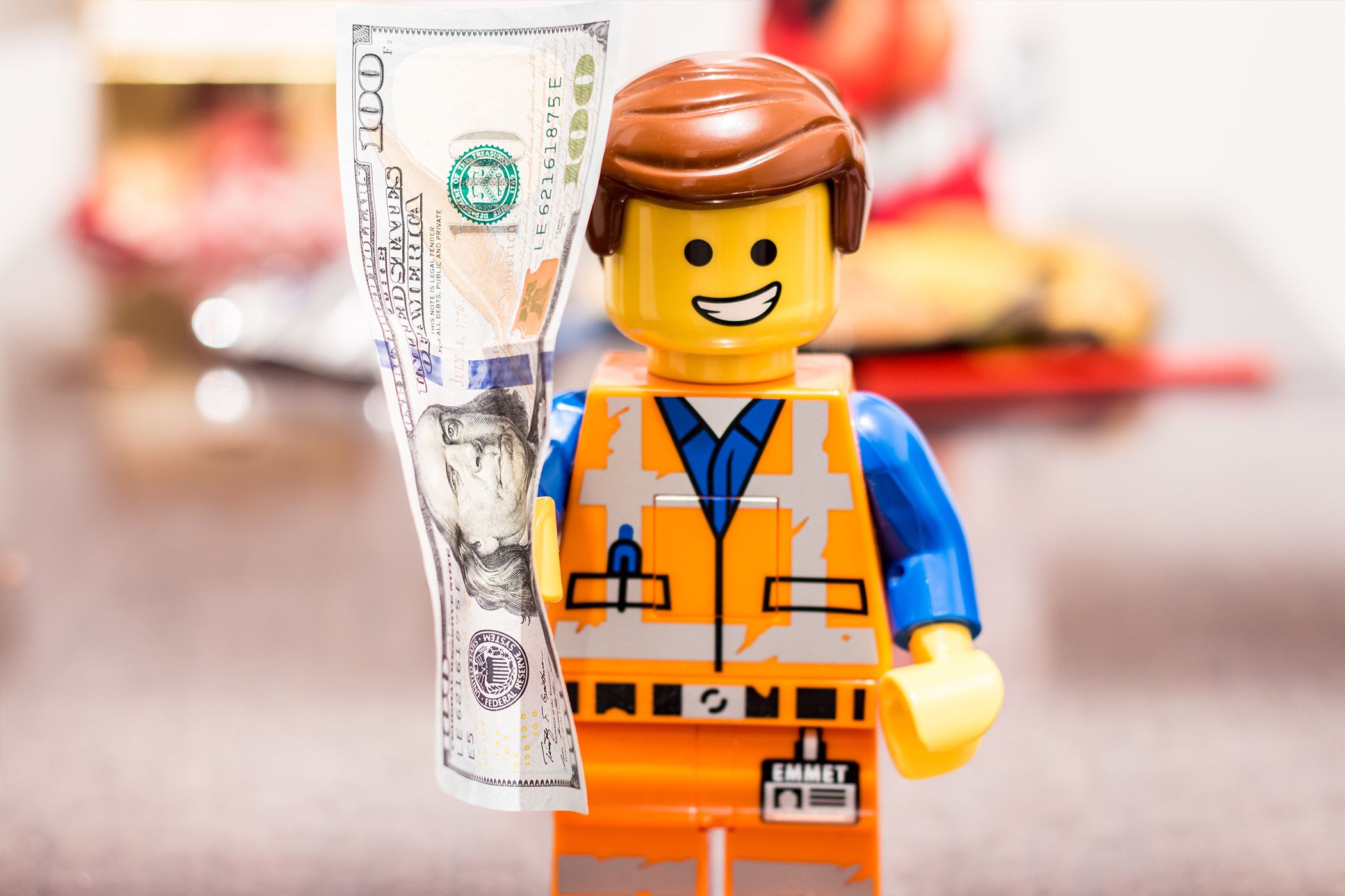 A LEGO figure holding a hundred dollar bill.