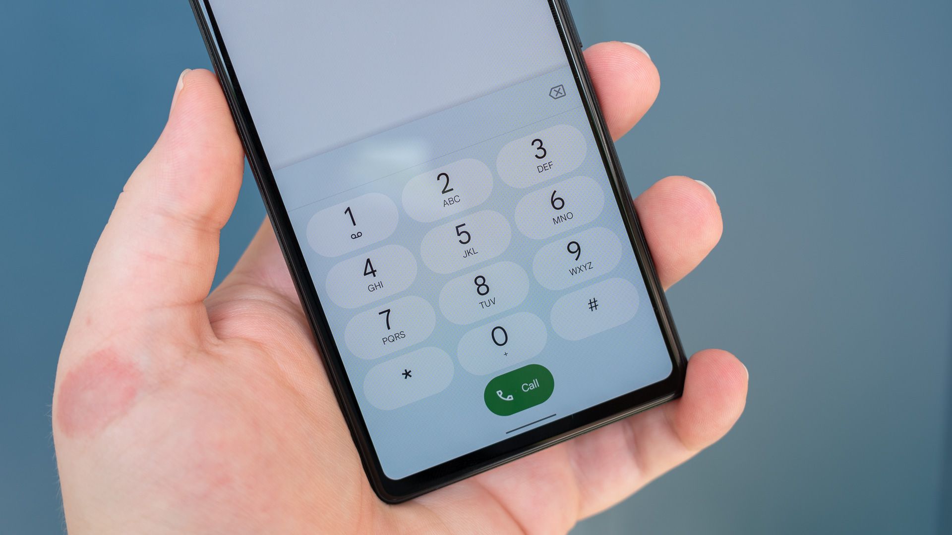 Person's hand holding the Google Pixel 6a with its phone dialer on-screen.