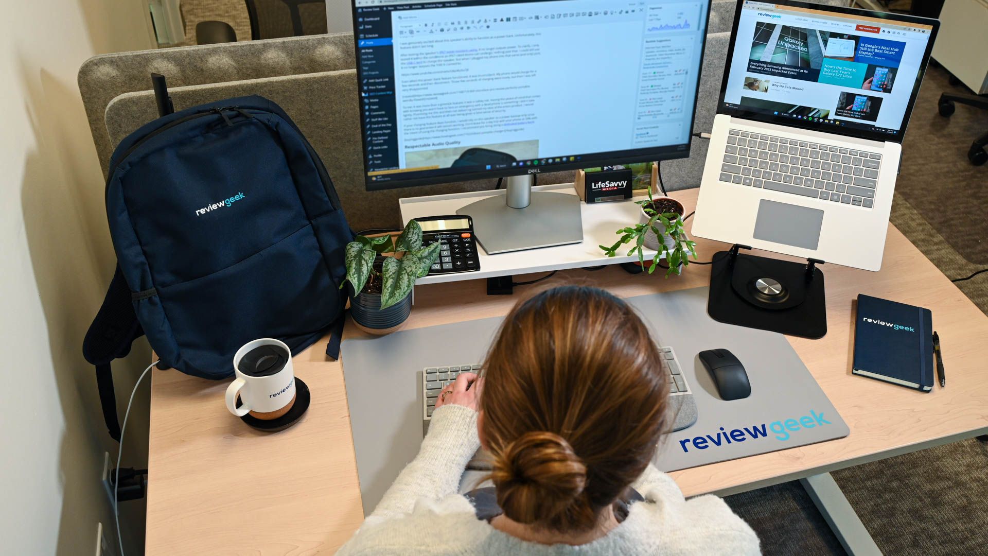 Person sitting at a desk typing on a computer with a connected laptop on a stand.