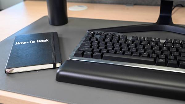 The Kensington QuietType Pro Silent Wireless Mechanical Keyboard with the wrist rest and a How To Geek notebook.