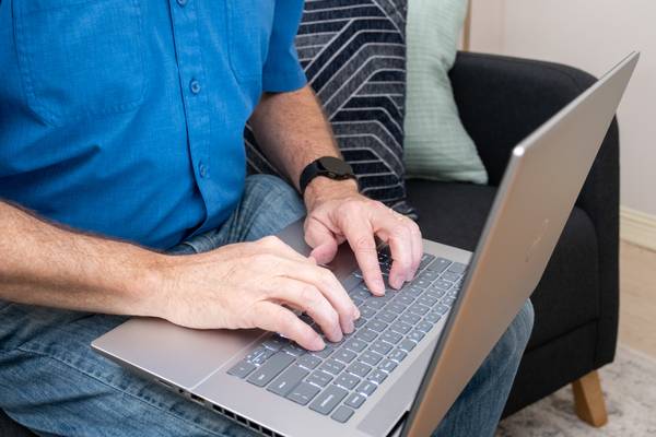 A man sitting on a couch types on a silver laptop.