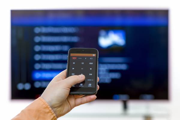 Closeup on woman hand holding smartphone and use a app with remote control and surfing programs on television.