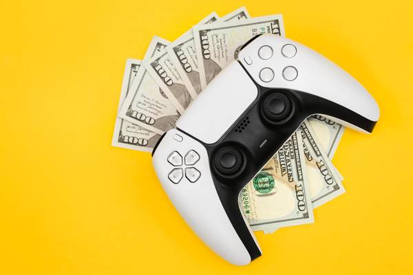 Five $100 bills under a PS5 controller.