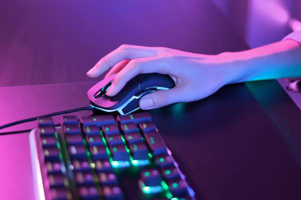 Person using a gaming mouse under pink neon lights next to an RGB keyboard.