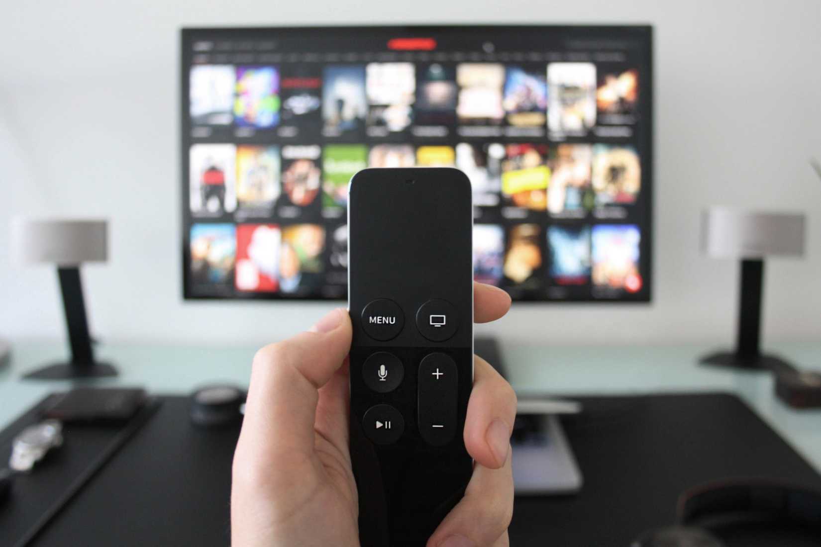 Hand holding a TV remote control while watching shows on a streaming service via Apple TV.