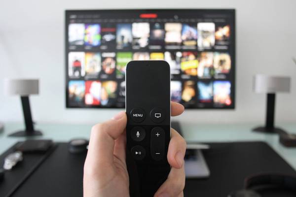 Hand holding a TV remote while watching shows on a streaming service via Apple TV.