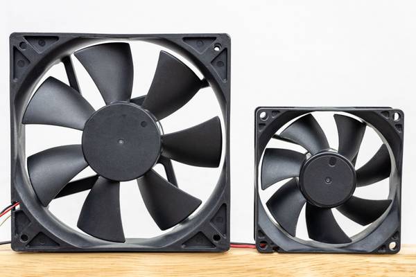 Two computer fans of different sizes sitting on a wooden floor against a white wall.