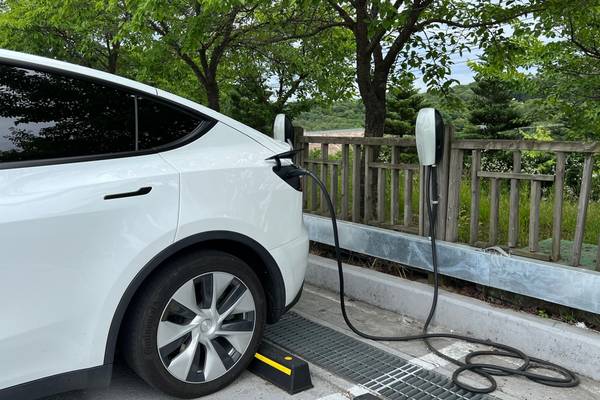 A Tesla destination charger at Yeoju Premium Outlet parking lot with a white car plugged in and charging.