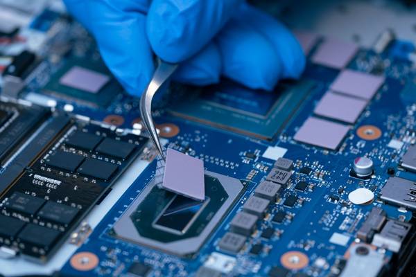 A person wearing gloves is using tweezers to install thermal paste on a computer chip.