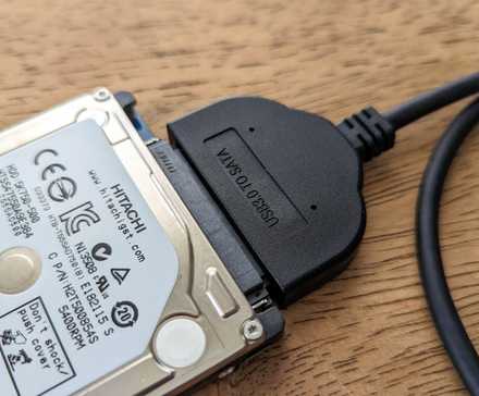 Hard drive connected to a USB adapter on a wooden surface.