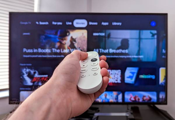 Person holding a Chromecast remote infront of a tv with Google TV open.