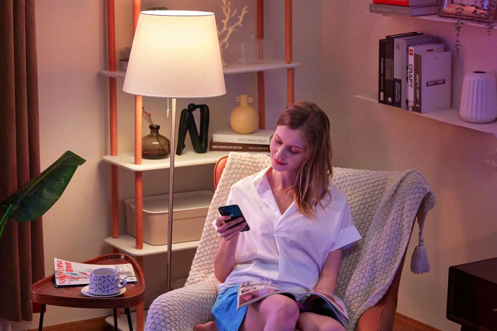 A woman sitting in a living room controlling a lamp using her smartphone.