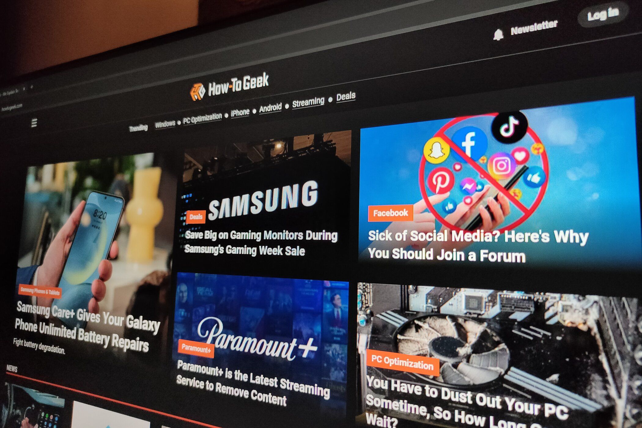 Le site Web How-To Geek en mode sombre affiché sur un moniteur dans une pièce faiblement éclairée.