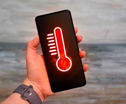 A hand holding a smartphone with a thermometer, indicating that the device is overheating.