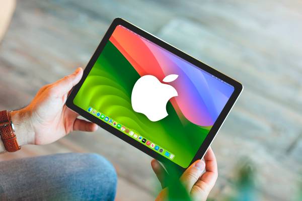 A hand holding an Ipad running MacOs and Apple logo on the screen