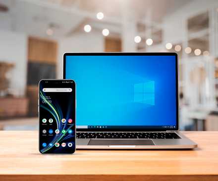 A notebook above a wooden desk with a windows screen and an android smartphone on the front left side-1