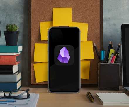 A smartphone on an office desk, with books, a laptop, and a wall with several notepads behind