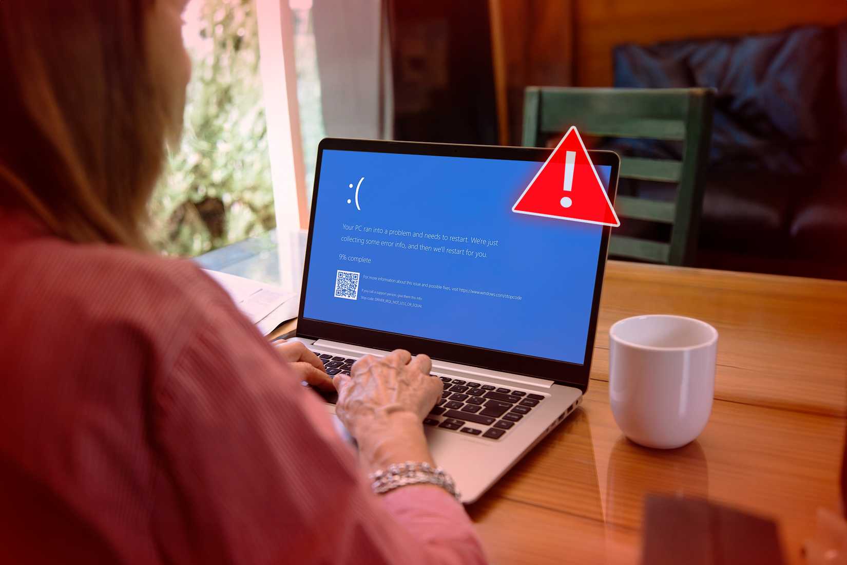 Uma mulher usando um laptop com uma tela azul que aparece quando o Windows é desligado aleatoriamente e um símbolo de alerta na frente do laptop